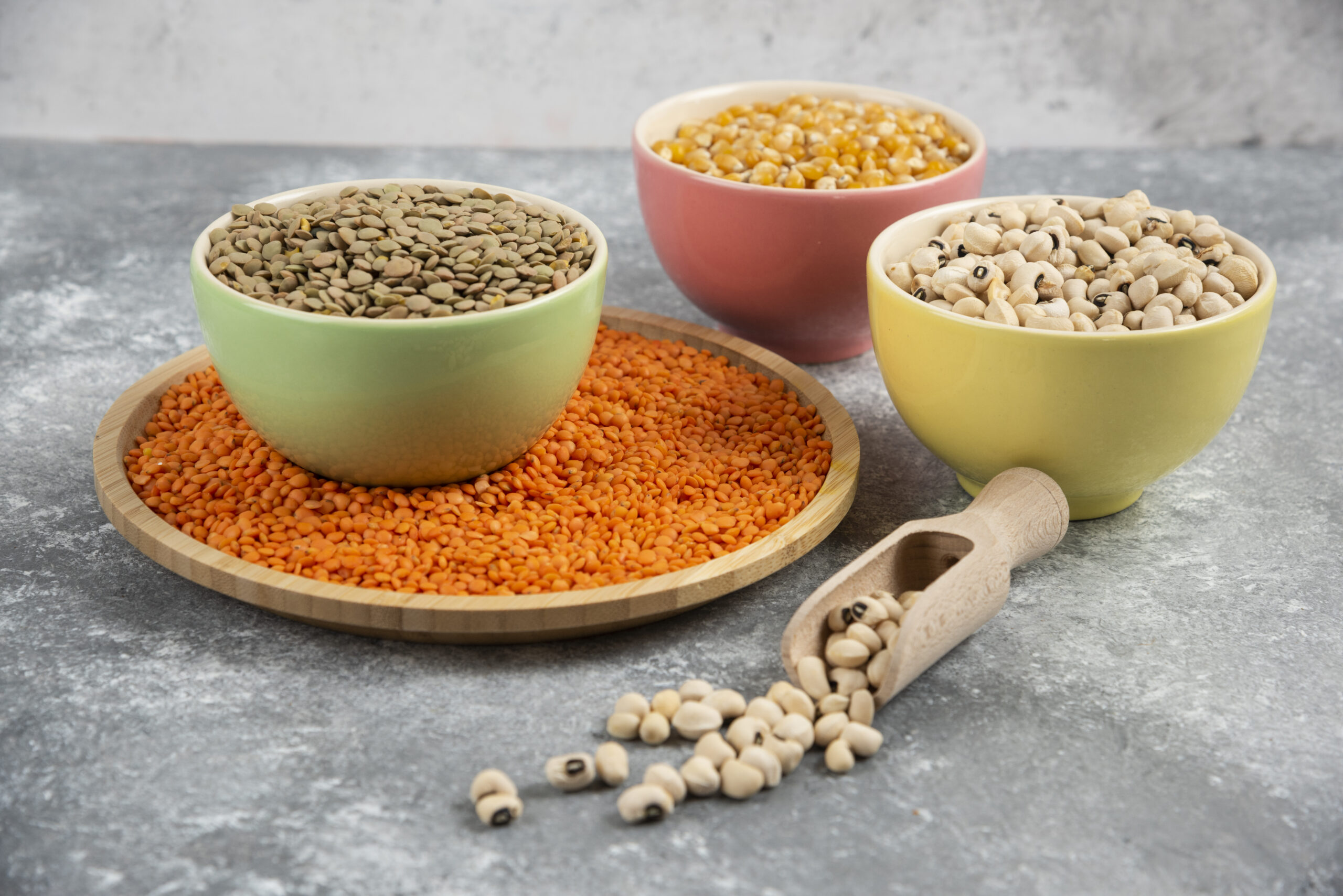 Colorful bowls of various uncooked beans, lentils and corns on marble surface
